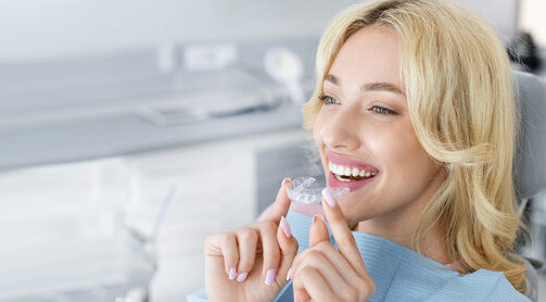A woman smiling while holding a clear aligner after an orthodontic appointment